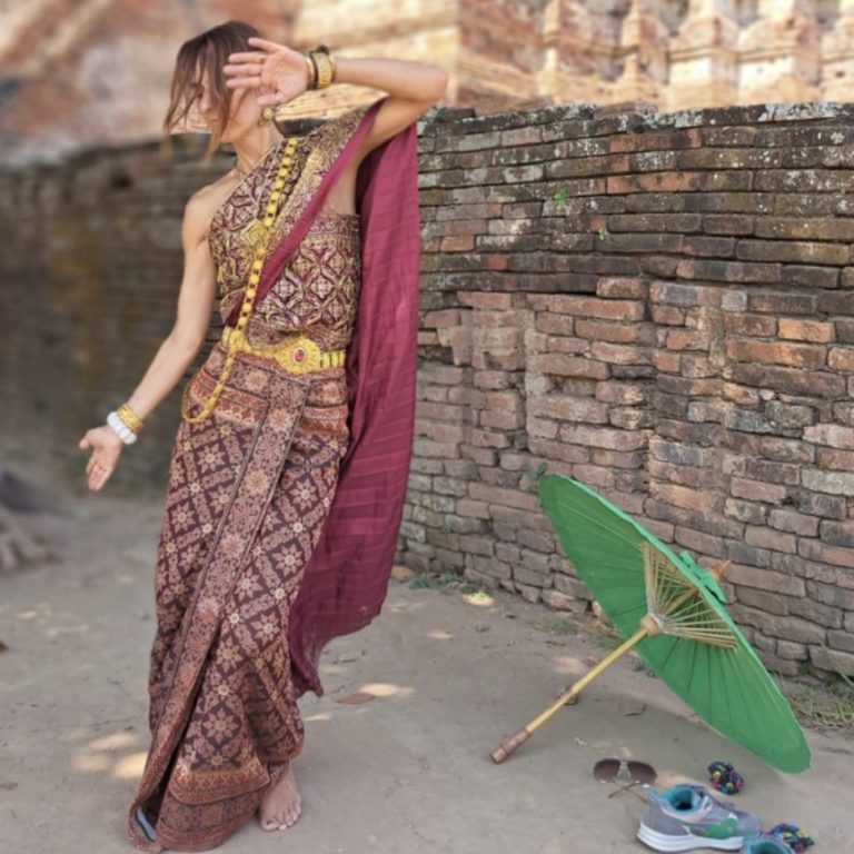 Britta Martin in traditioneller Thailändischer Kleidung Tanzend mit grünem Sonnenschirm, vor einer antiken Steinmauer.